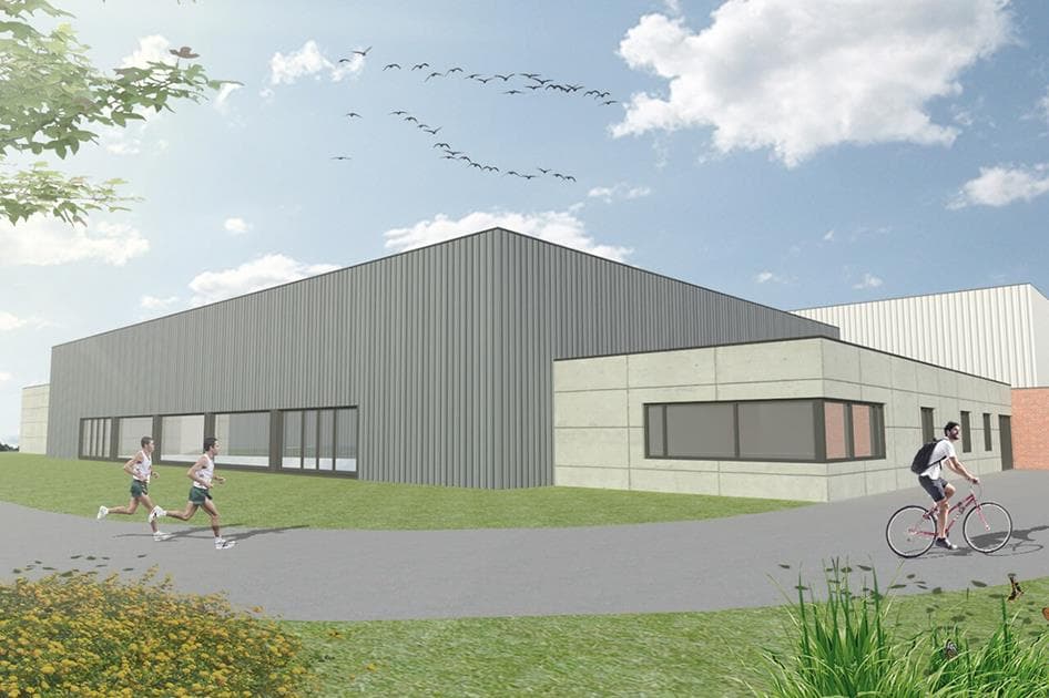 Sportcentrum De Veldmuis in Geraardsbergen: een grijze sporthal met lichte aanbouw, omringd door gras.